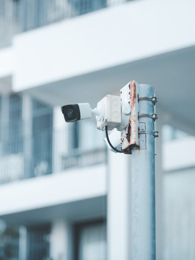 CCTV equipment mounted to post outside white apartment building
